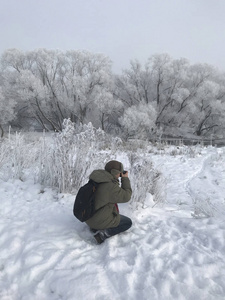 摄影师用他的相机拍摄冬天的风景。 冬季公园。 灌木丛和树木覆盖着厚厚的霜冻。