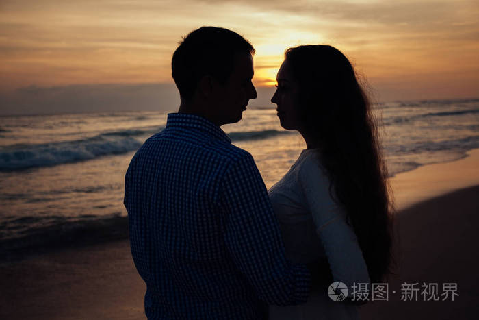 两个年轻的恋人站在海滩上在日落的背景下互相看着对方夫妇爱