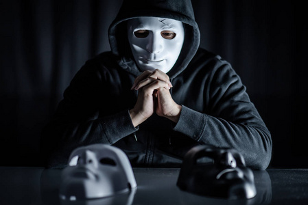 帽衫男戴着神秘面具,在桌子上选择黑色或白色面具. 匿名社交伪装.