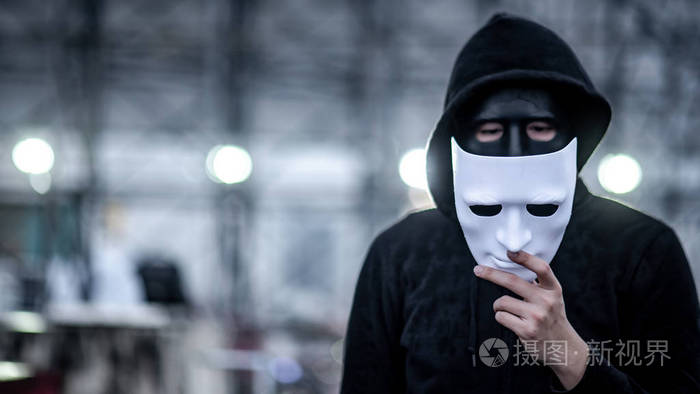 神秘的帽衫男子打破黑色面具手中拿着白色面具匿名社会掩蔽或双相情感