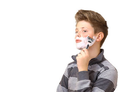 一个十几岁的年轻人在刮胡子。 孤立在白色背景上。 在剃刀的手里。 胡须上的泡沫。 文本的地方。