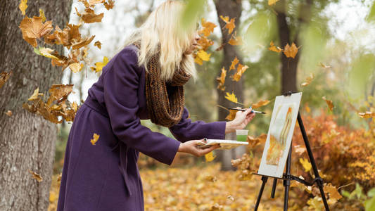 金发碧眼的女艺术家画在落叶在秋天公园