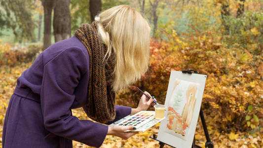 在秋园画架上画一幅画的年轻女艺术家特写镜头