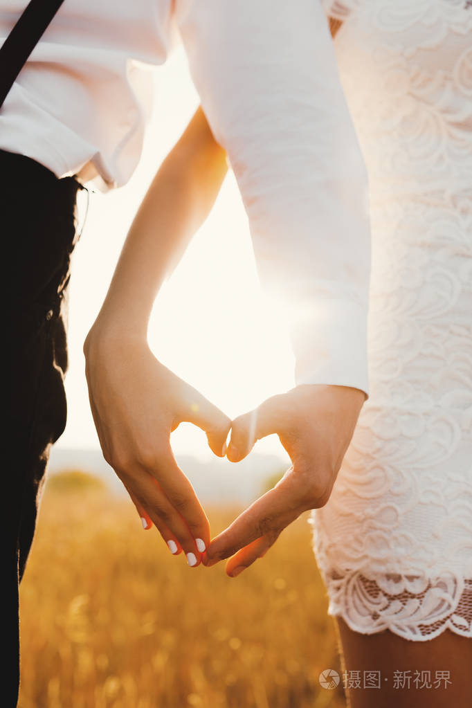 亲密的男人和女人用手在金色草地背景上明亮的阳光下做心.