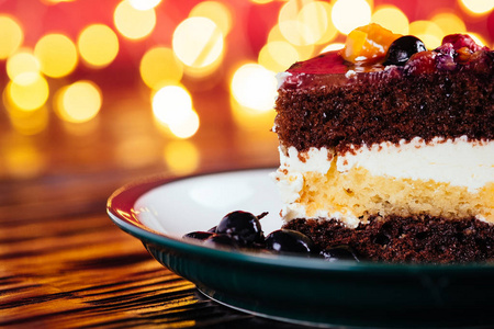 一块蛋糕，加奶油巧克力水果，木制和红色背景的甜甜点，还有bokeh灯