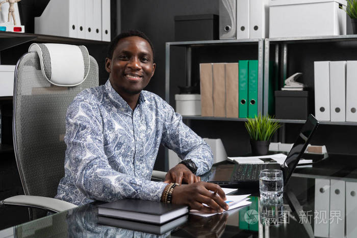 美丽的年轻非洲裔美国商人的肖像与文件和笔记本电脑在办公室工作