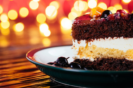 一块蛋糕，加奶油巧克力水果，木制和红色背景的甜甜点，还有bokeh灯