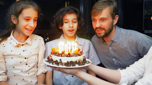 快乐的微笑男孩在她的生日蛋糕上吹蜡烛。被家人包围的孩子。带蜡烛的生日蛋糕。