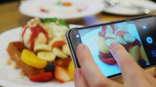 特写。女性手中的智能手机上的智能手机上拍摄了维也纳华夫饼冰淇淋和新鲜水果的甜点