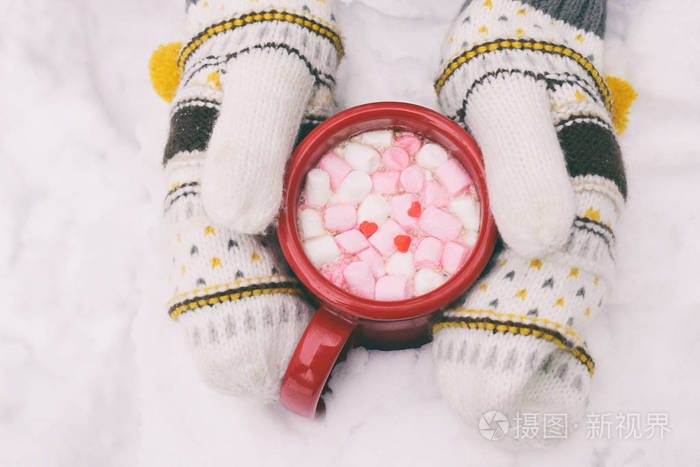 女人手拿着一杯热巧克力和棉花糖。 针织手套和热可可饮料。 你好，二月或情人节的概念。