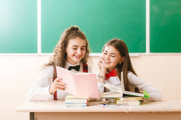 两个布伦特学校的女生坐在教室的课桌旁黑板的背景上放着书