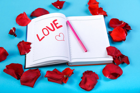 在玫瑰花瓣的设计中, 用红色的毛毡笔写在蓝色背景的笔记本上的爱这个词