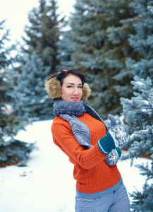 女人在冬天的森林里摆姿势，美丽的风景和雪杉树。 穿着红色毛衣和耳罩