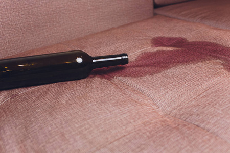 红酒洒在棕色沙发上。黑葡萄酒瓶下降