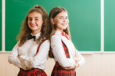 两个穿着红色校服的深色女学生站在教室里,在黑板的背景下看书,玩得很