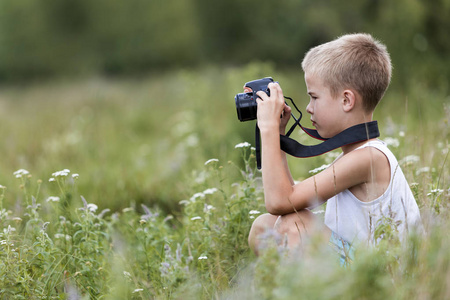个人资料特写照片，年轻的金发可爱的英俊的孩子男孩与相机拍摄户外阳光明媚的春天或夏天在模糊的浅绿色草地复制空间背景。