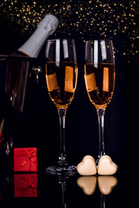 香槟瓶，两个酒杯和两个心形巧克力在黑色背景与金光。 爱情情人节概念