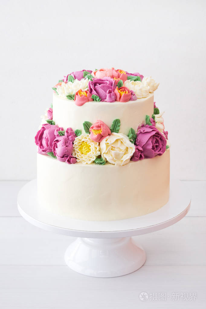 两层白色婚礼蛋糕装饰彩色奶油花在白色的木制背景.