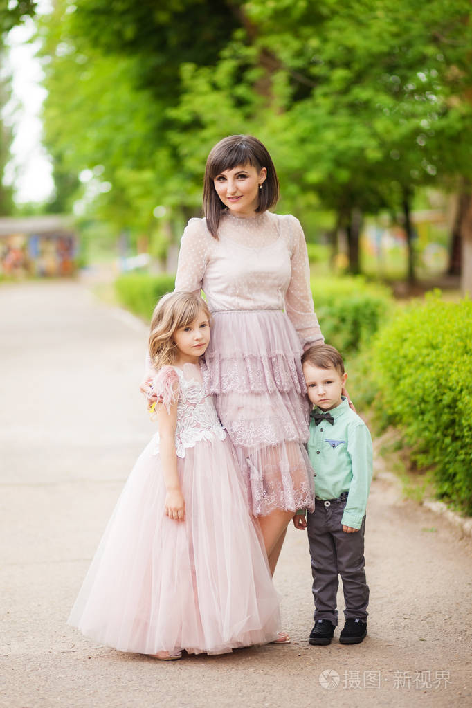 母亲带着女儿穿着米色,郁郁葱葱的衣服,儿子穿着绿色衬衫,在夏天的绿