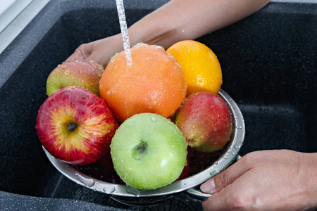 水洗水果一个女人在厨房里用自来水洗水果.照片