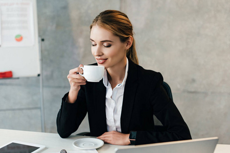 有魅力的女商人坐在工作场所时，喜欢闭着眼睛喝咖啡