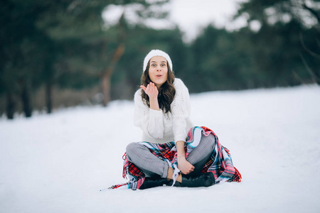 一个年轻的女人坐在雪地里，在冬天的森林里散步时，脸上带着惊喜。