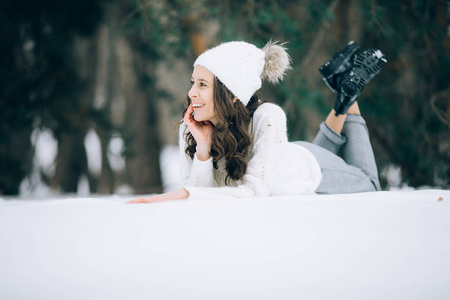 年轻开朗的女人在冬天的森林里散步时躺在雪地上微笑。