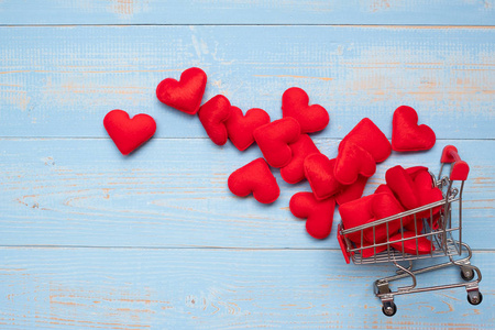 顶部视图红色心形装饰与迷你购物车蓝色木桌背景。爱情浪漫购物情人节概念