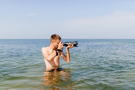 一位年轻的游客带着相机站在海上