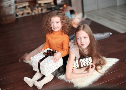 两个小妹妹带着礼品盒, 坐在一个舒适的客厅里的地板上