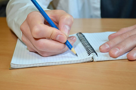 s hand in a white shirt writes the text with a blue pensil in a 