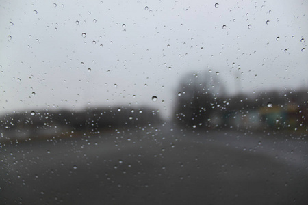 雨点落在玻璃特写上。 在模糊的背景树和房子上