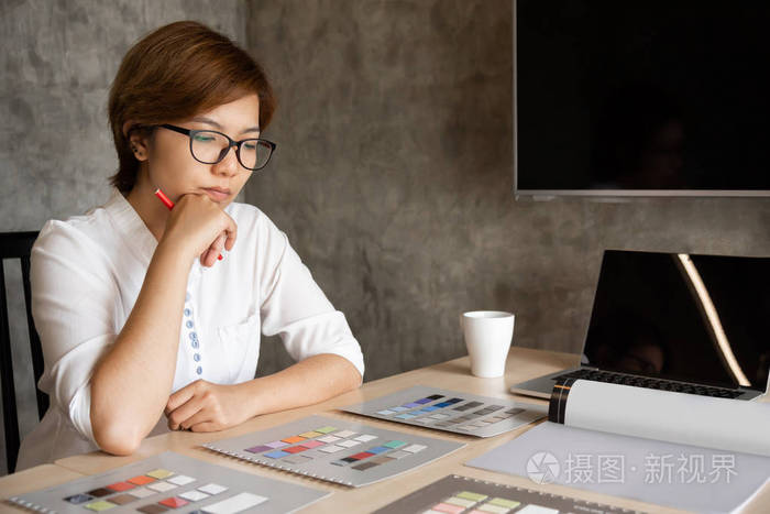 亚洲女设计师坐着思考. 有思想的建筑师女性牵着下巴,看着她的作品.