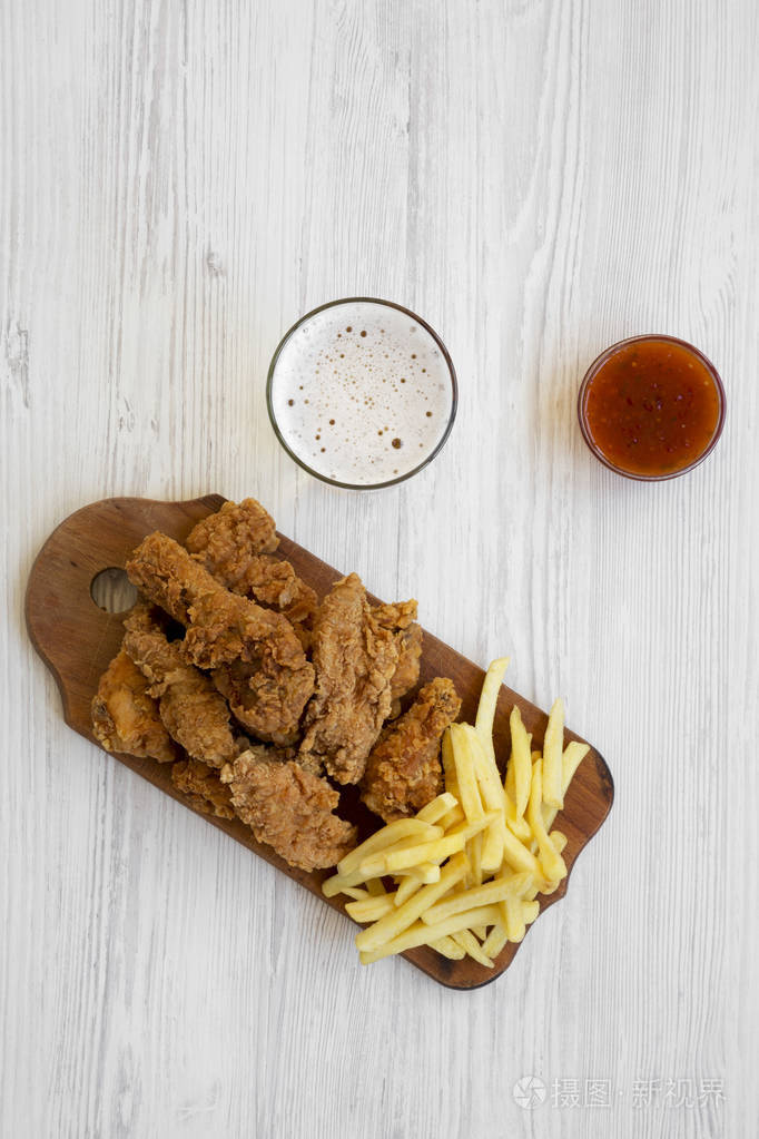 美味的快餐:炸鸡腿,辣翅,炸薯条和鸡条加酸甜酱和冷啤酒覆盖白色木制