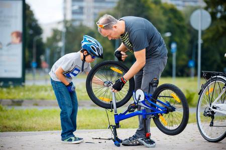 可爱的小男孩和他的父亲在户外修理自行车