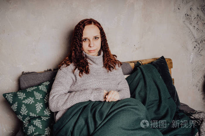一个穿毛衣的年轻女孩坐在床上蜷缩在毯子里女人穿着温暖的毛衣街头