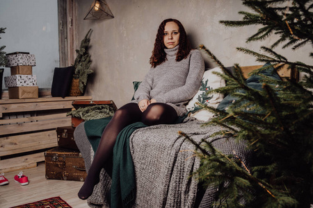 女孩蜷缩一个穿着毛衣坐在床上的年轻女孩蜷缩在毯子里.