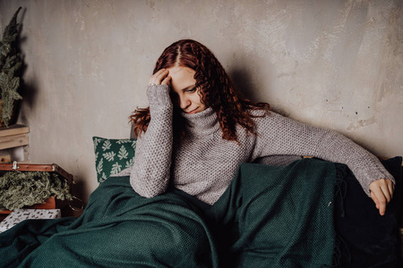 坐在女孩蜷缩一个穿着毛衣坐在床上的年轻女孩蜷缩在毯子里.