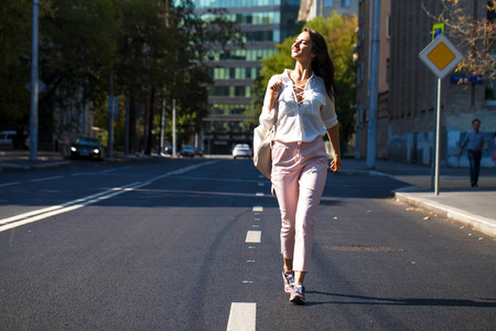 穿着白色上衣和粉红色裤子的年轻美丽的黑发女人在夏天的户外街头散步