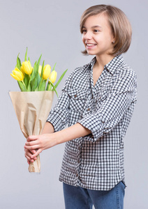 灰色背景上有一束花的漂亮女孩。 带着黄色郁金香花束的微笑的孩子作为礼物。 母亲生日快乐或情人节快乐。