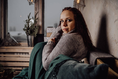 蜷缩的人一个穿着毛衣坐在床上的年轻女孩蜷缩在毯子里.