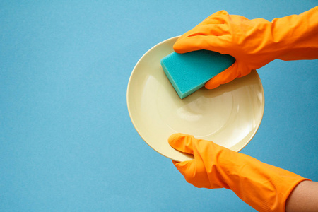 s hands in orange protective gloves with plate and sponge on blu