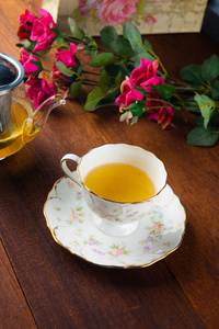 近景玻璃茶壶和一杯新鲜热茶放在木制桌面上，上面有粉红色的花
