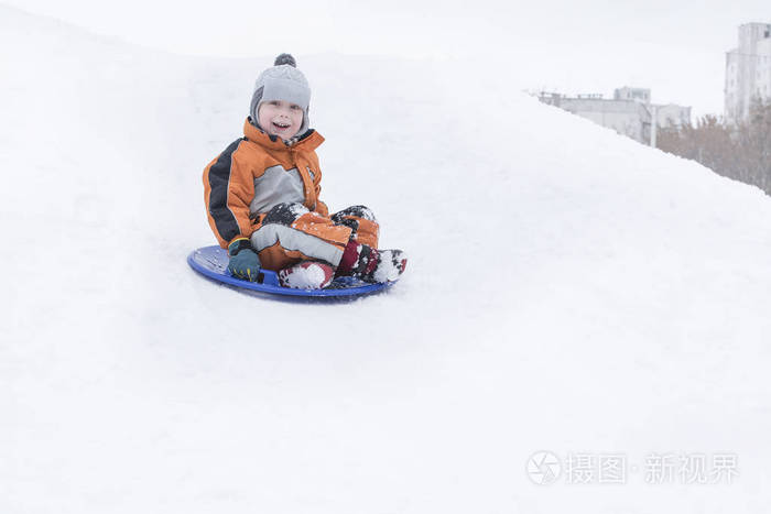 开心地笑着的小男孩在雪碟上滑下山。 季节性概念。 冬季