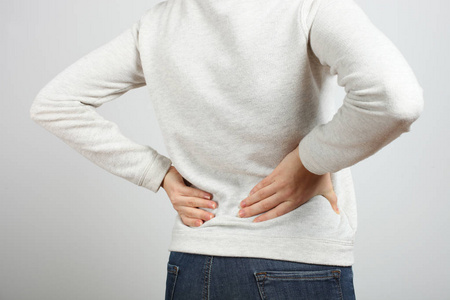 腰痛的患病妇女站在中立的背景上。