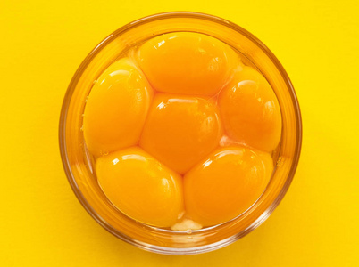 六个一半六个生鸡蛋放在玻璃碗里,打蛋器靠近蛋黄,在黄色背景上分离