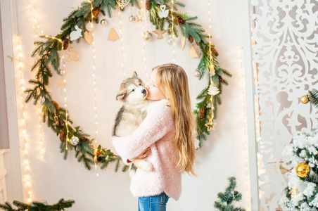 一个可爱的女孩，一头金发，在家里和一只可爱的小狗玩耍，房间里装饰着圣诞节