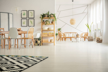 白色墙壁的几何图案在明亮的开放式平面内，客厅里有木制桌子和椅子和藤条家具