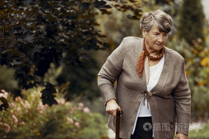 在公园散步时拿着手杖的老妇人