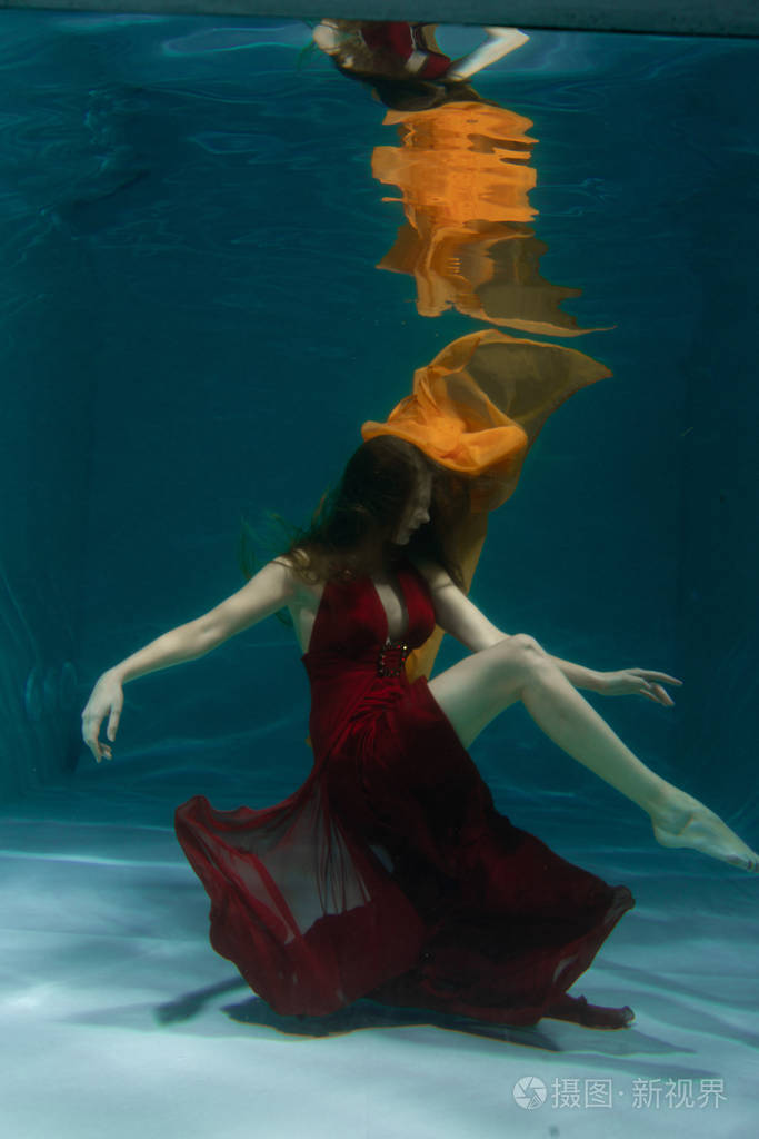 一个美丽的自由潜水员,一个人穿着红色的长裙,独自在深水中游泳